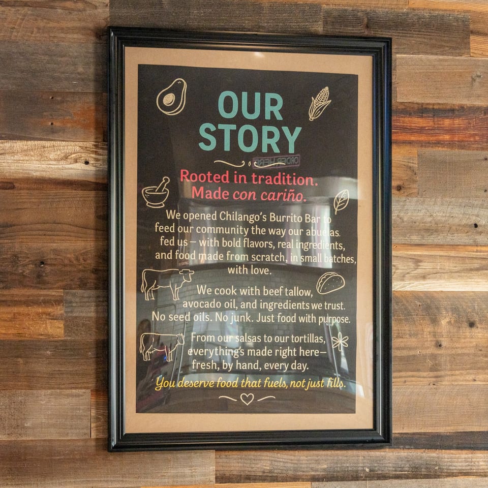 Chilango's Burrito Bar's "Our Story" sign on a rustic wooden wall, detailing their food philosophy.
