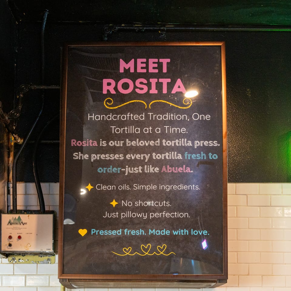 A chalkboard sign at Chilango's Burrito Bar introduces "Rosita," their tortilla press, and highlights fresh ingredients.